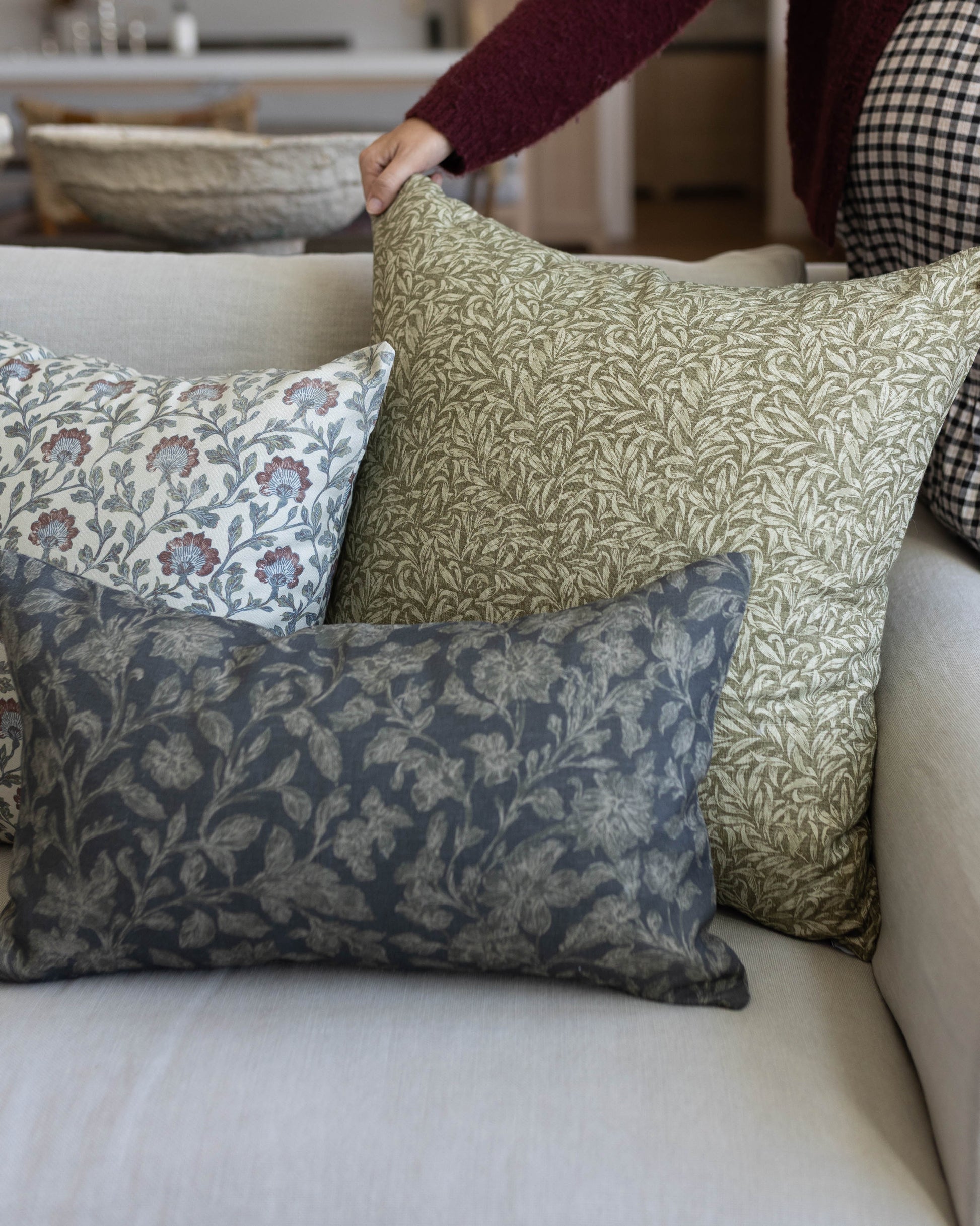 Green leaf-patterned throw pillow displayed on a cream sofa with coordinating floral pillows.