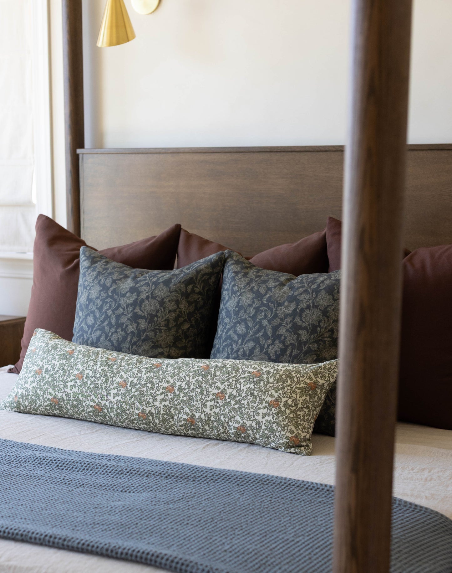 Bed with wooden frame displaying decorative pillows including patterned gourd and ivy design in green and neutral tones.