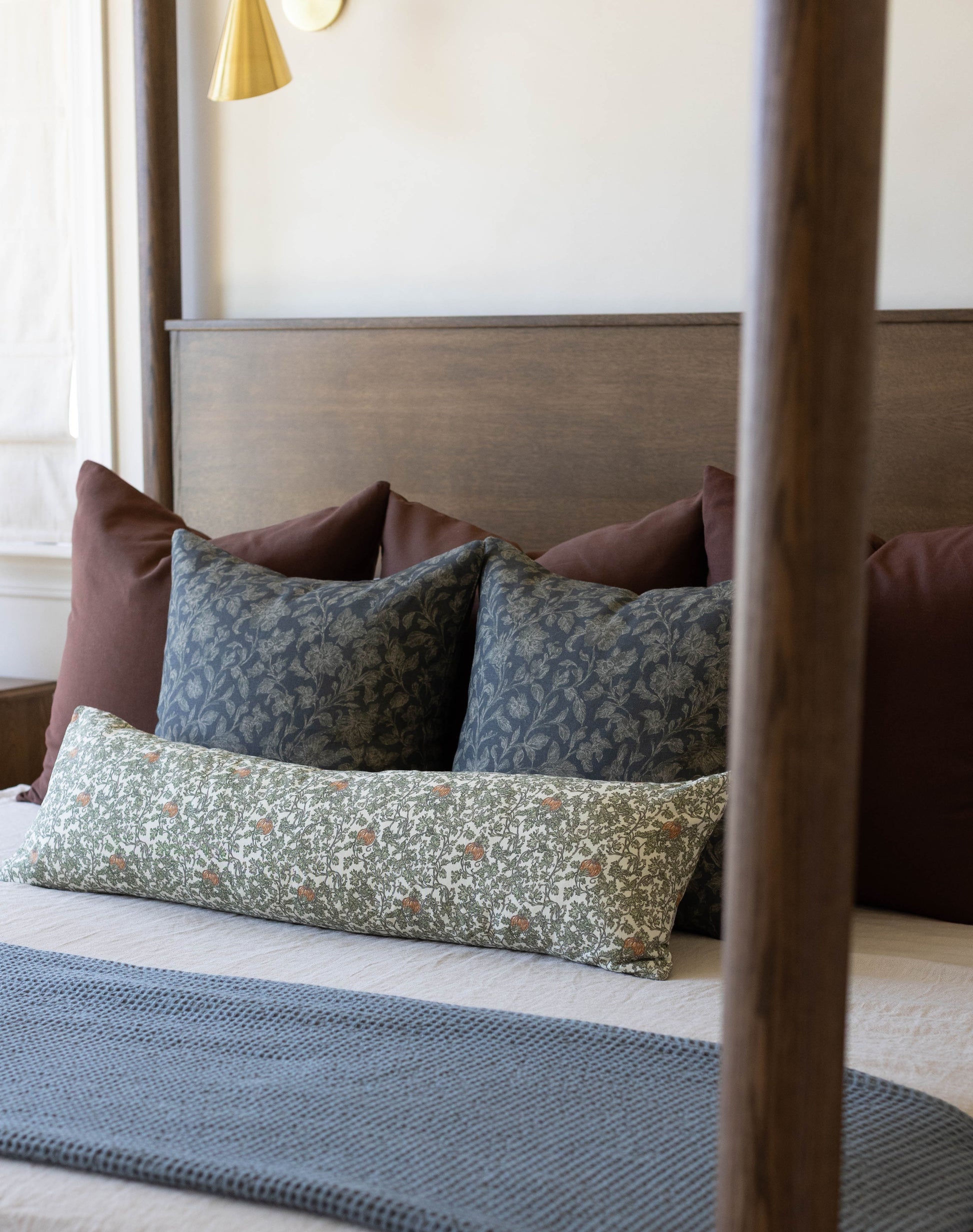 Bed with wooden frame displaying decorative pillows including patterned gourd and ivy design in green and neutral tones.