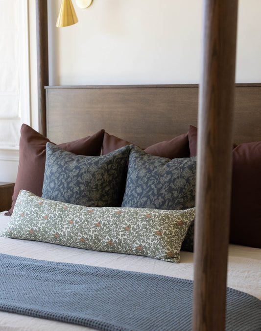 Bed with wooden frame displaying decorative pillows including patterned gourd and ivy design in green and neutral tones.