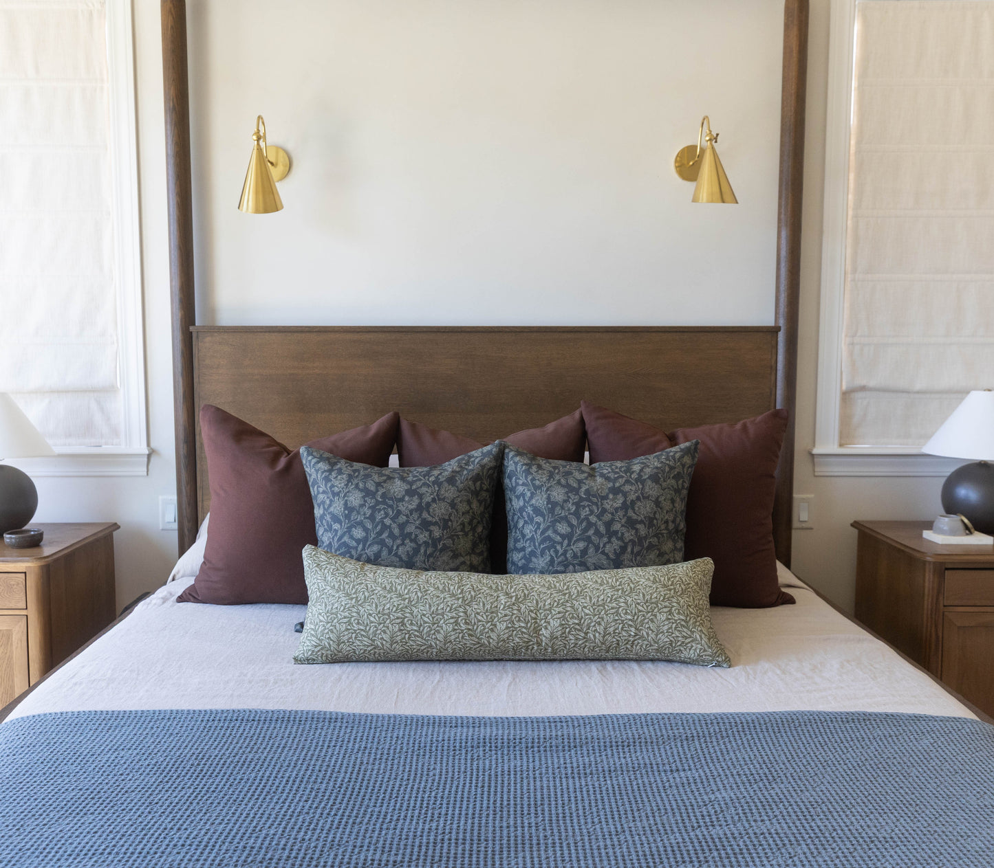 Bedroom with four-poster bed, decorative pillows, wooden nightstands, and two brass wall sconces above headboard.