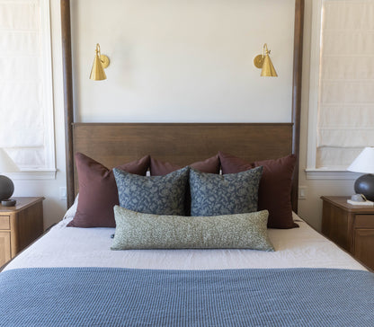 Bedroom with four-poster bed, decorative pillows, wooden nightstands, and two brass wall sconces above headboard.