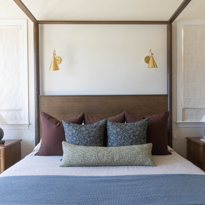 Four-poster bed with brown wooden frame, white headboard panel, and brass cone sconces on either side.