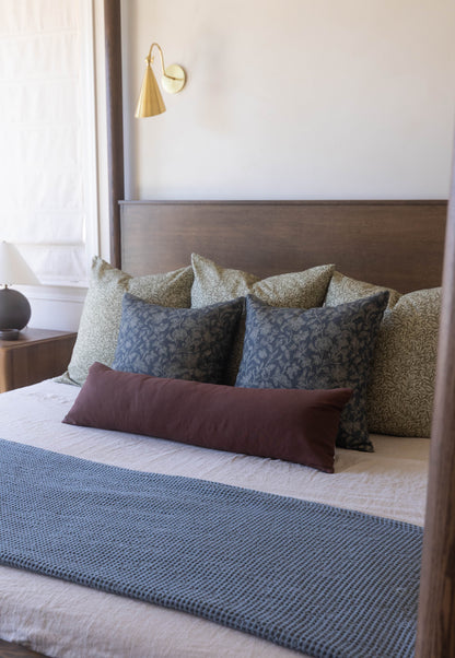 Bed with taupe upholstered headboard styled with patterned throw pillows in beige and blue tones and burgundy lumbar pillow.