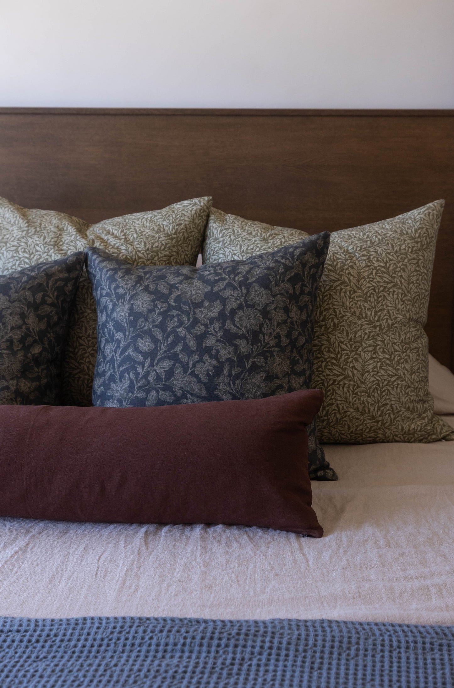 Decorative pillows in blue, tan, and burgundy damask patterns arranged on a bed with brown headboard.