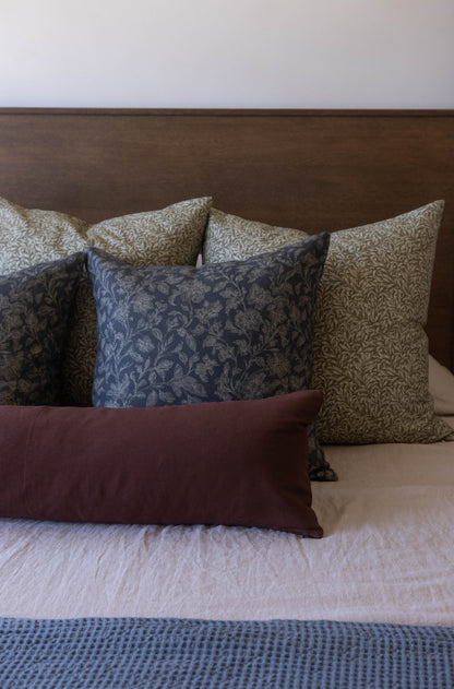 Decorative pillows in blue, tan, and burgundy damask patterns arranged on a bed with brown headboard.