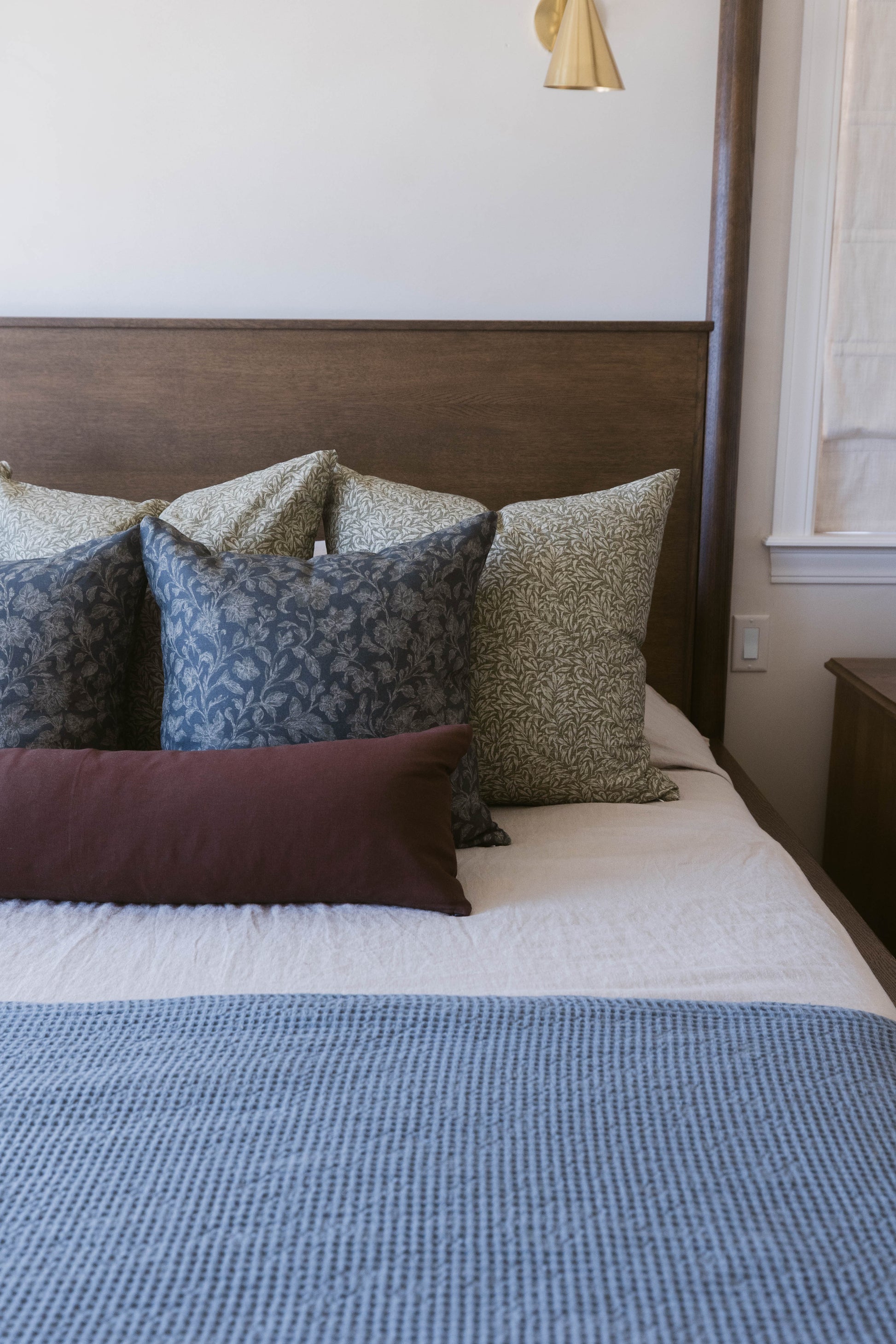 Green and blue patterned throw pillow displayed on a bed with burgundy and neutral pillows.