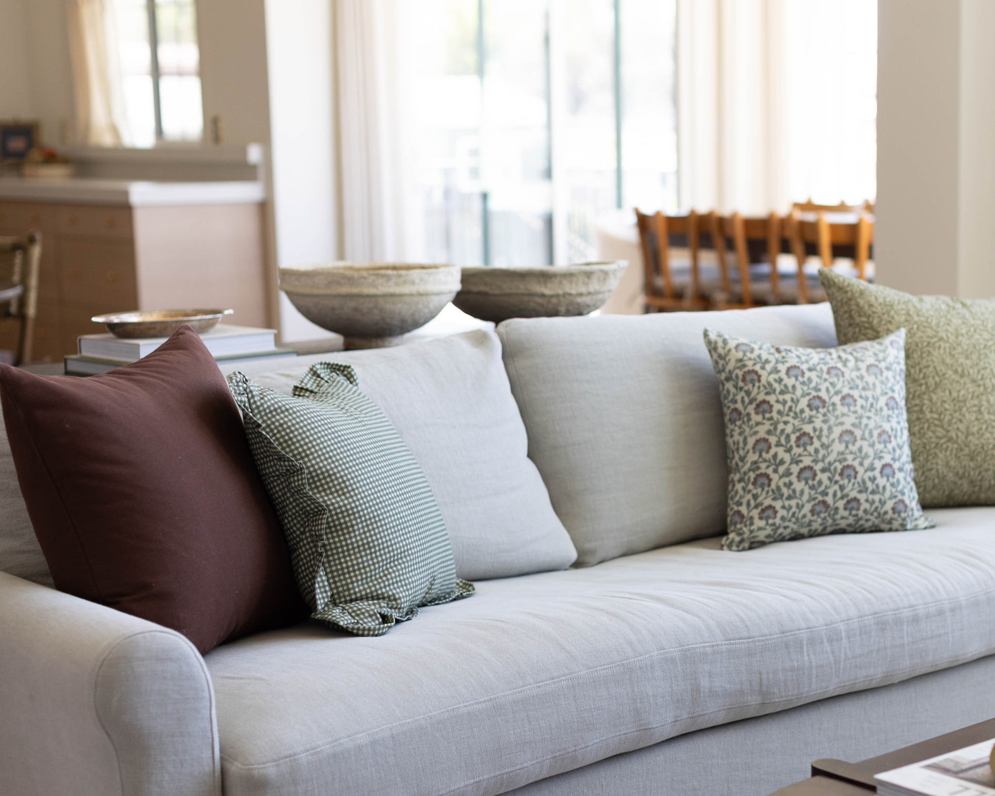 Light gray upholstered sofa with burgundy, checkered, white, and patterned accent pillows in a bright living room.