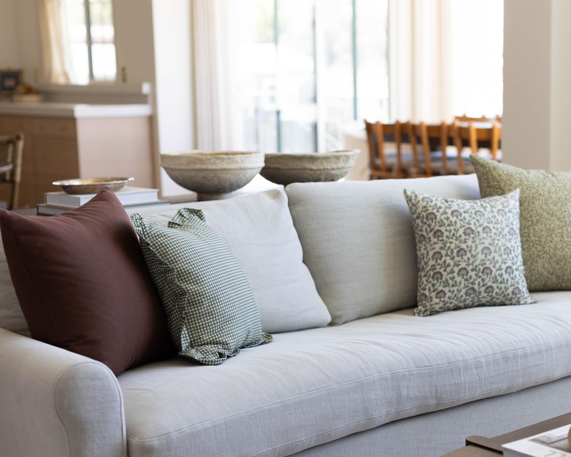 Light gray upholstered sofa with burgundy, checkered, white, and patterned accent pillows in a bright living room.