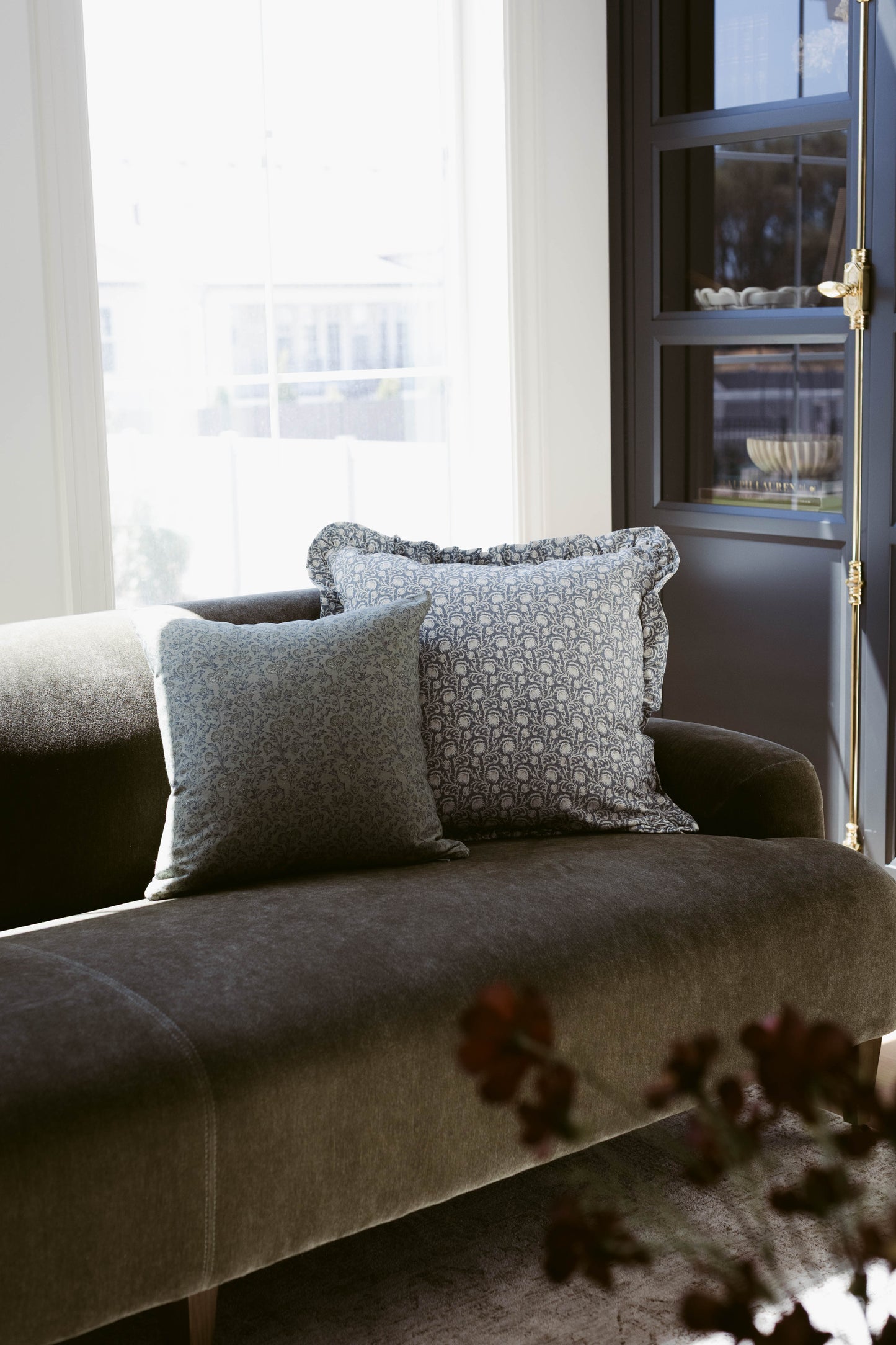 Two gray decorative pillows with ruffle edges on a charcoal upholstered chair by a window.