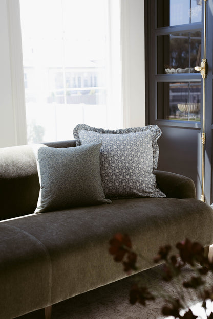 Two gray decorative pillows with ruffle edges on a charcoal upholstered chair by a window.