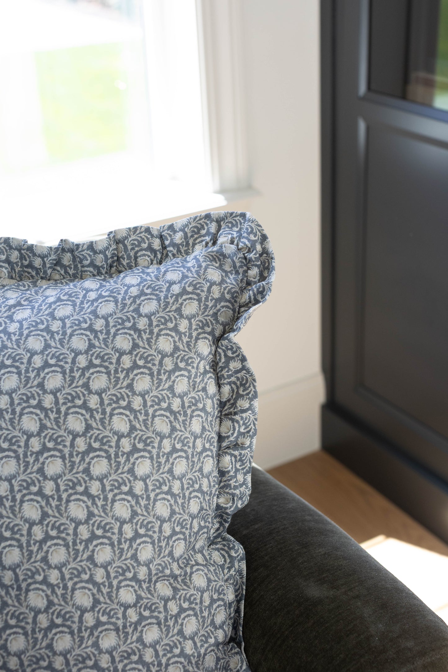 Blue and cream damask patterned pillow with ruffled edges displayed on furniture by a window.