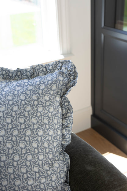 Blue and cream damask patterned pillow with ruffled edges displayed on furniture by a window.