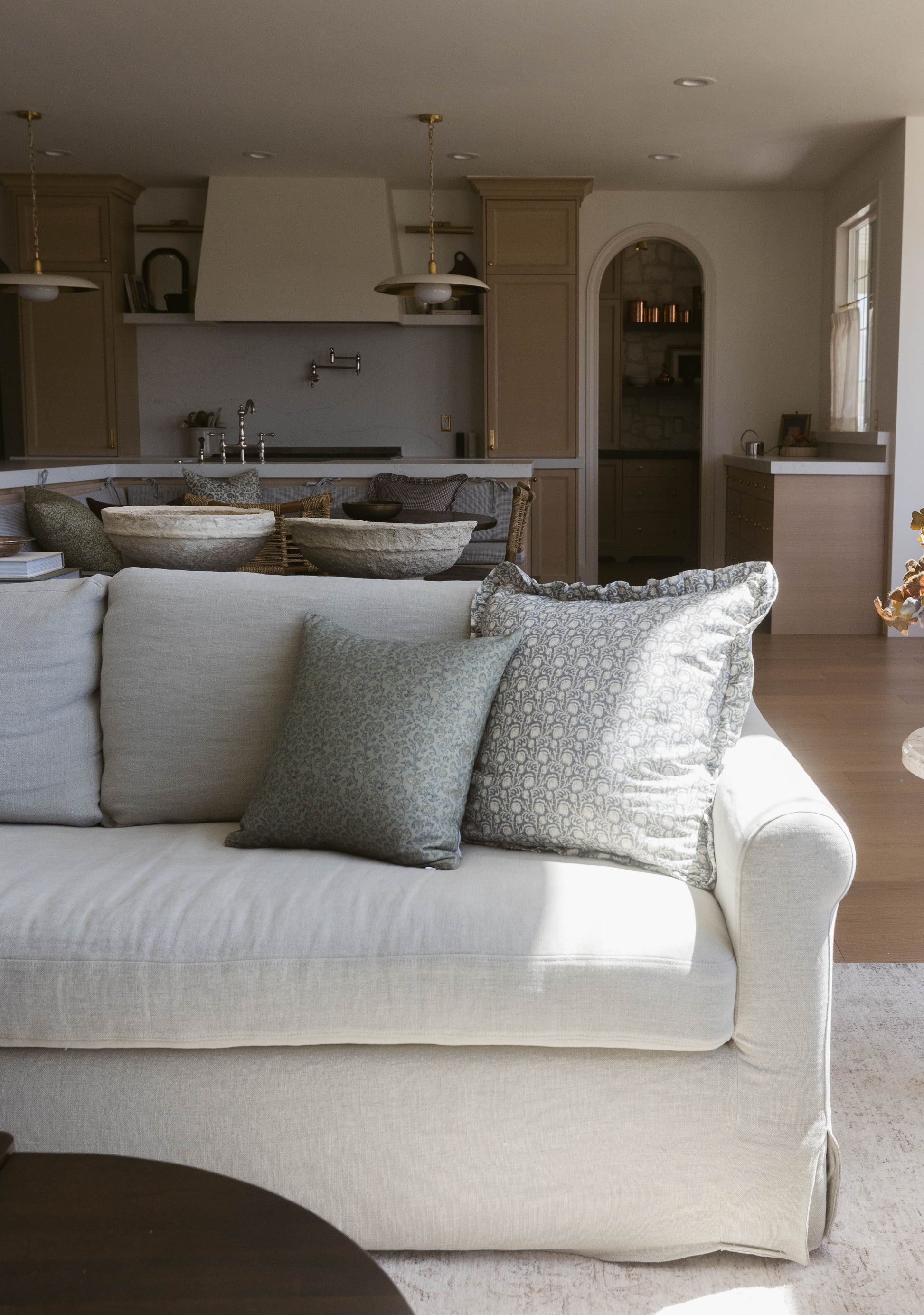 Cream upholstered sofa with ruffled skirt and two patterned throw pillows in a living room setting.