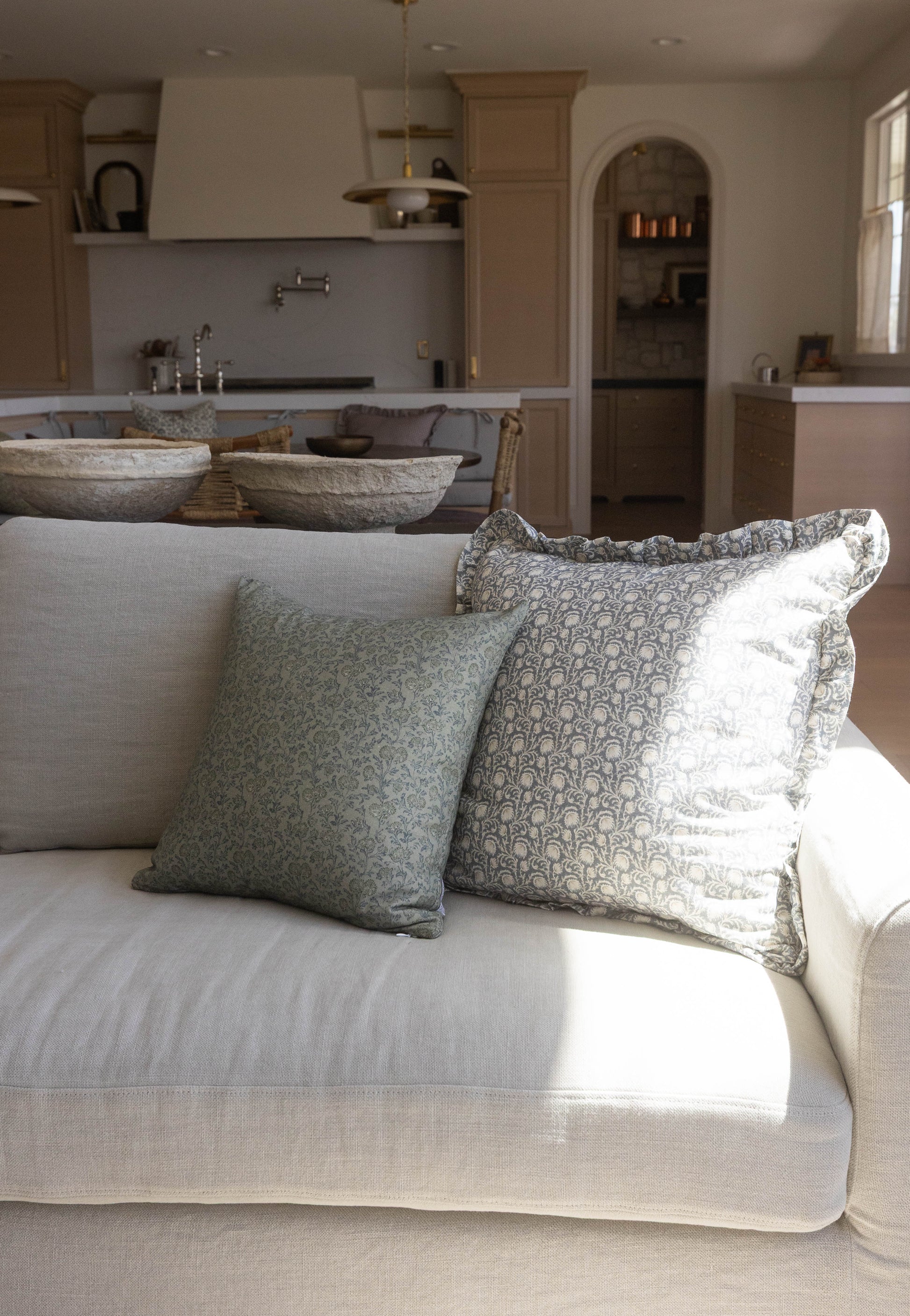 Green and cream patterned pillows with ruffled edges arranged on a light gray upholstered sofa.