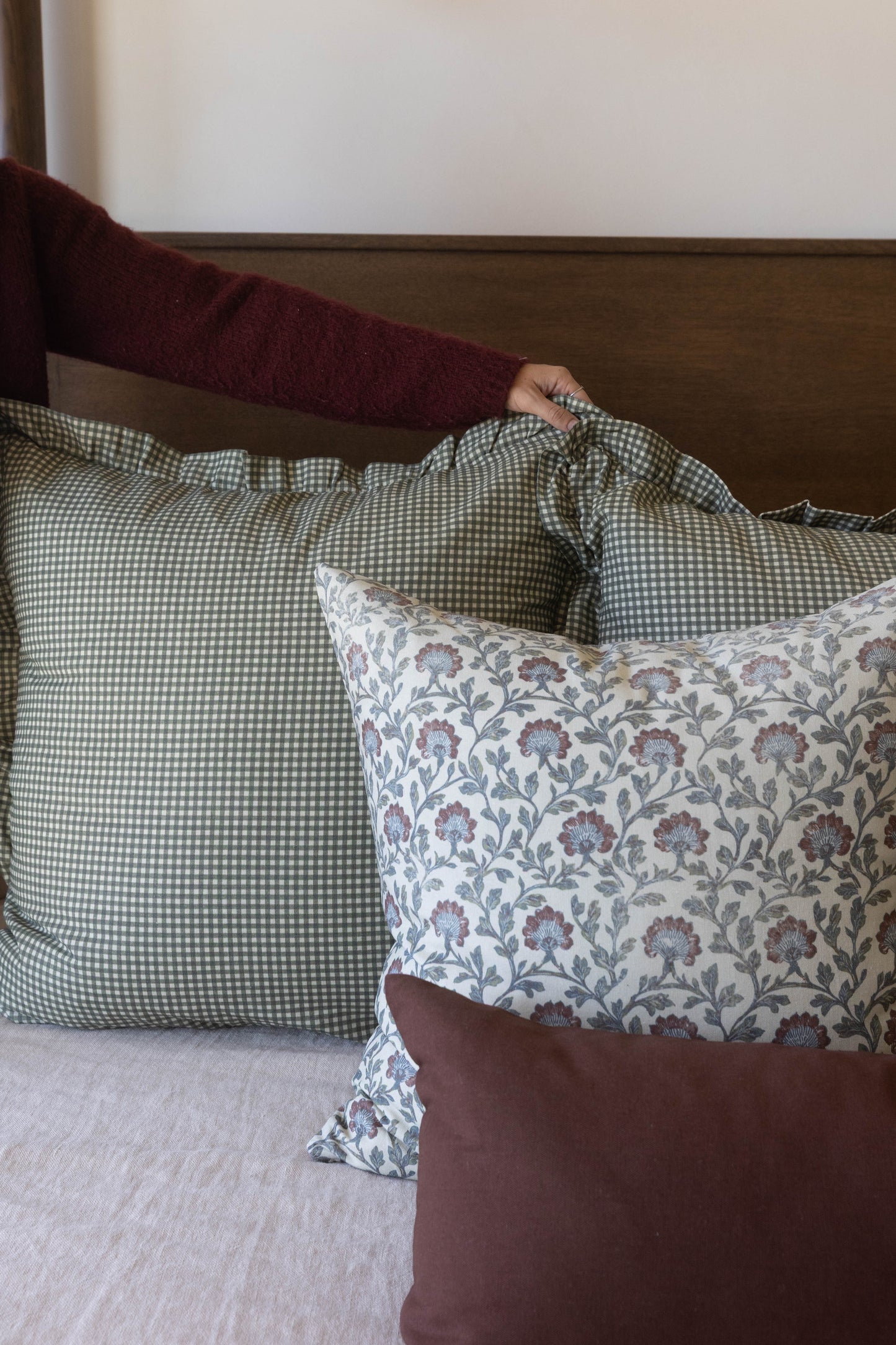 Multicolor decorative pillow with floral and gingham patterns displayed on a bed with coordinating pillows.