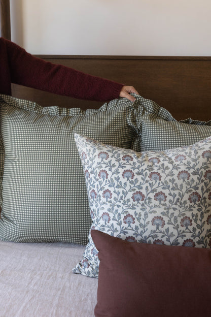 Multicolor decorative pillow with floral and gingham patterns displayed on a bed with coordinating pillows.