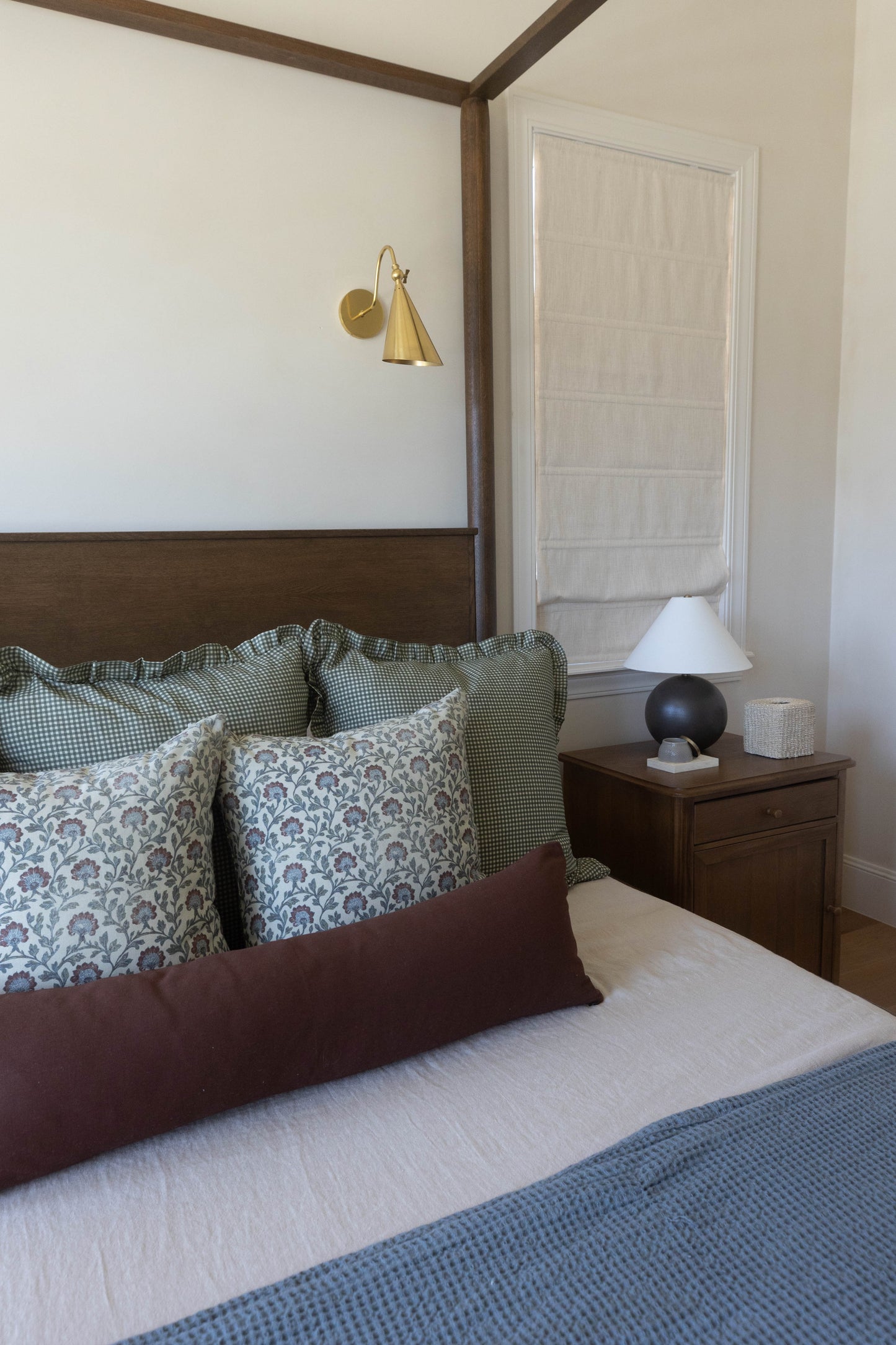 Bedroom with four-poster bed, patterned pillows, brass wall sconce, wooden nightstand with lamp, and white closet door.