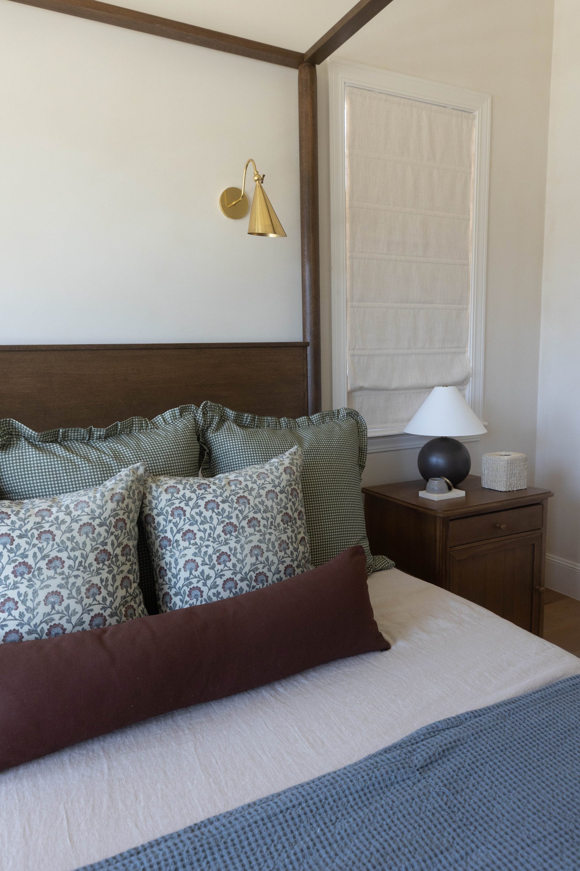 Bedroom with four-poster bed, patterned pillows, brass wall sconce, wooden nightstand with lamp, and white closet door.