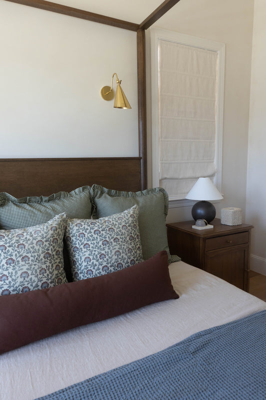 Bedroom with four-poster bed, patterned pillows, brass wall sconce, wooden nightstand with lamp, and white closet door.