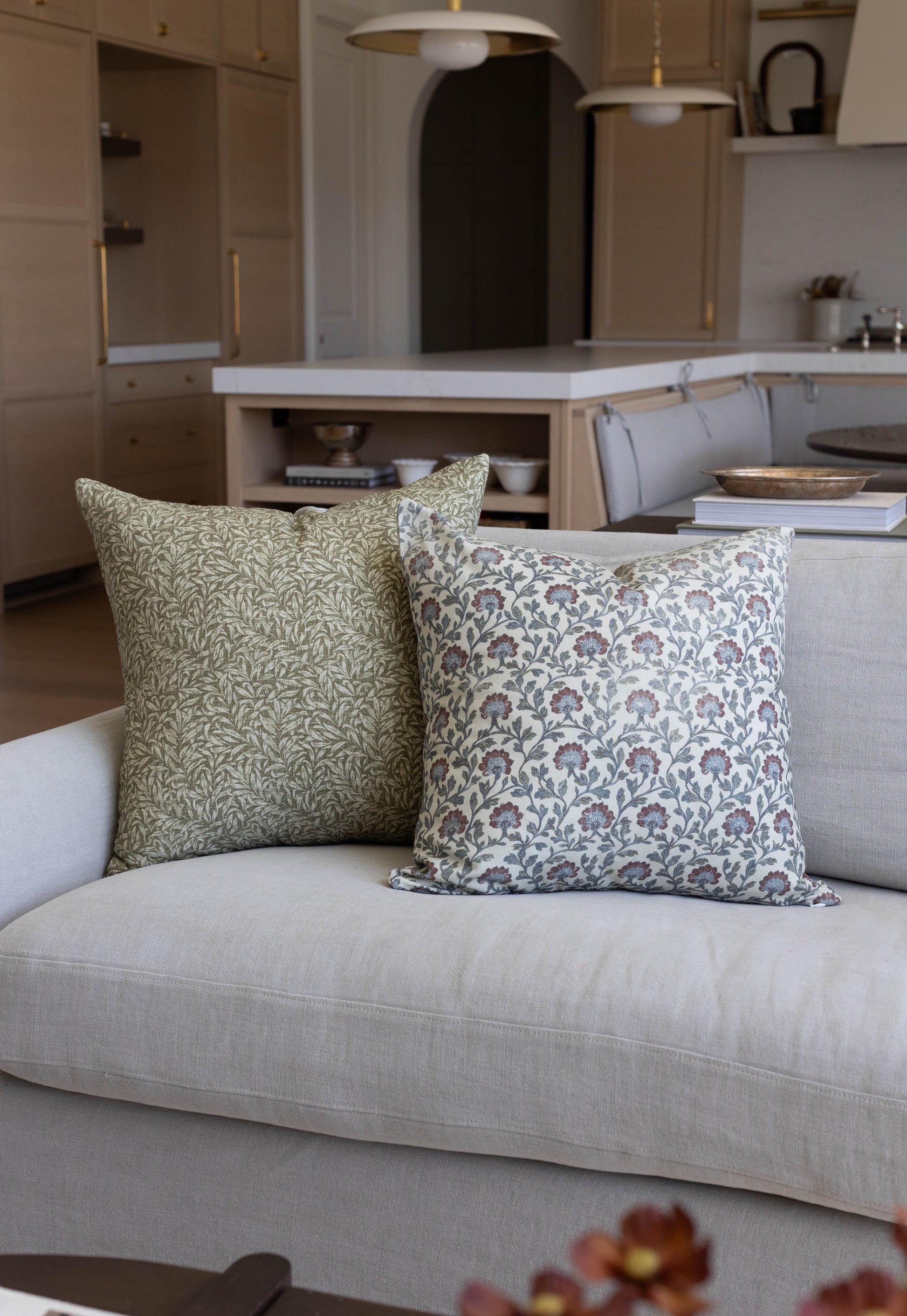 Two decorative pillows with floral and botanical print patterns in green and cream tones on a light gray sofa.