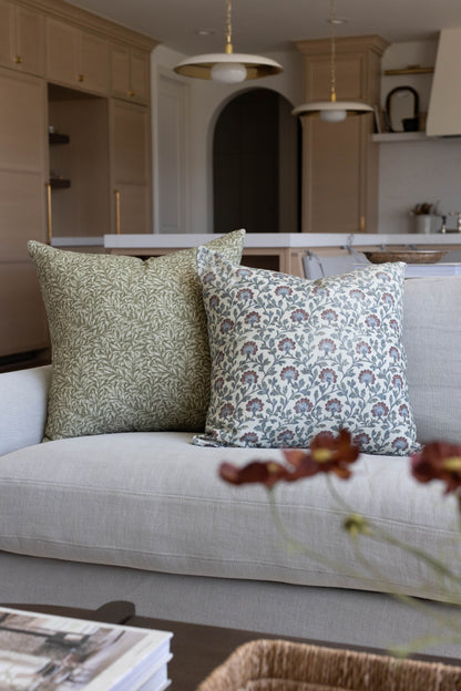 Two multicolor patterned throw pillows with floral and leaf designs in sage and blue tones on a cream sofa.