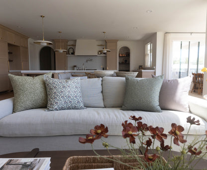 Four decorative pillows in varying patterns displayed on a light gray sofa in a modern kitchen and living space.