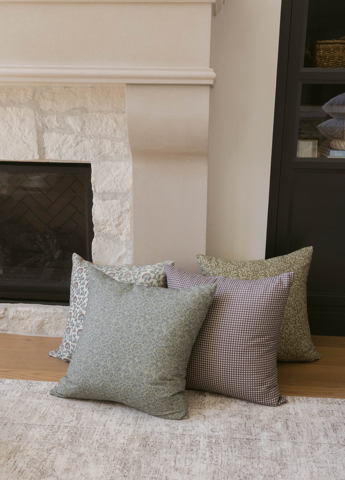 Green and mauve patterned throw pillows displayed on a light rug in front of a fireplace.