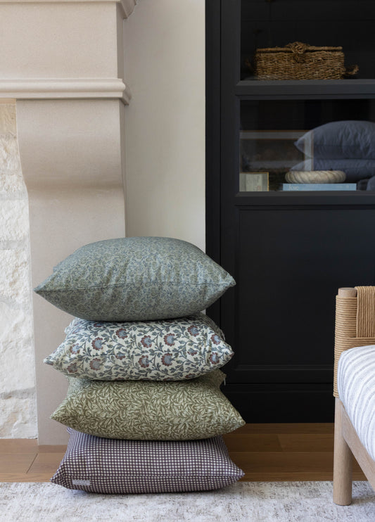Four stacked throw pillows in varying patterns: solid gray-blue, floral, leafy green, and gingham check.