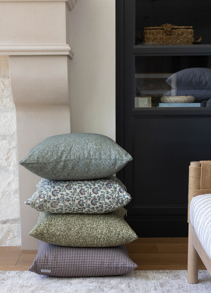 Four stacked green throw pillows with varying patterns displayed on a bedroom floor.