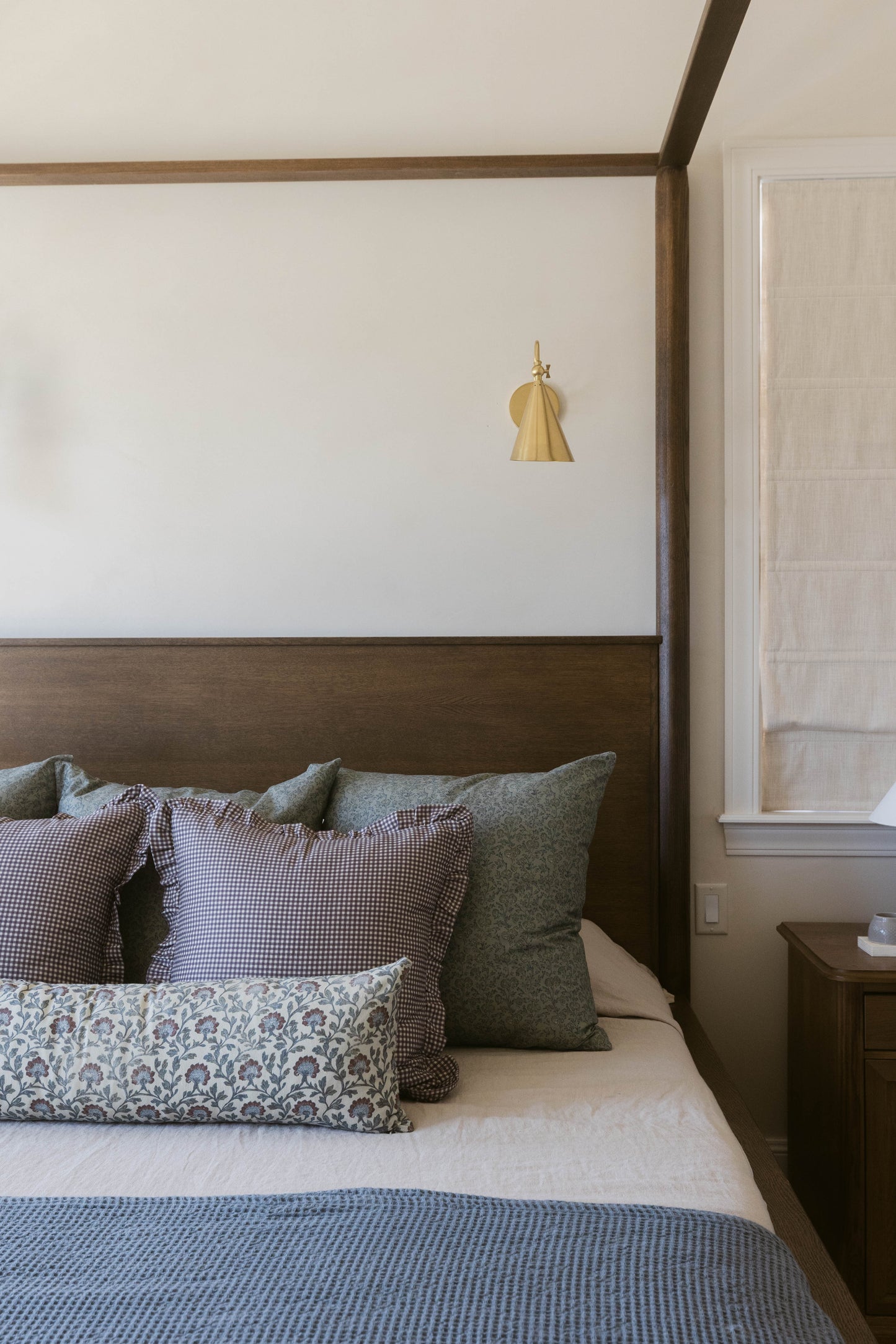 Brass pendant lamp with pleated cone shade hanging above a wooden four-poster bed with multicolored pillows.