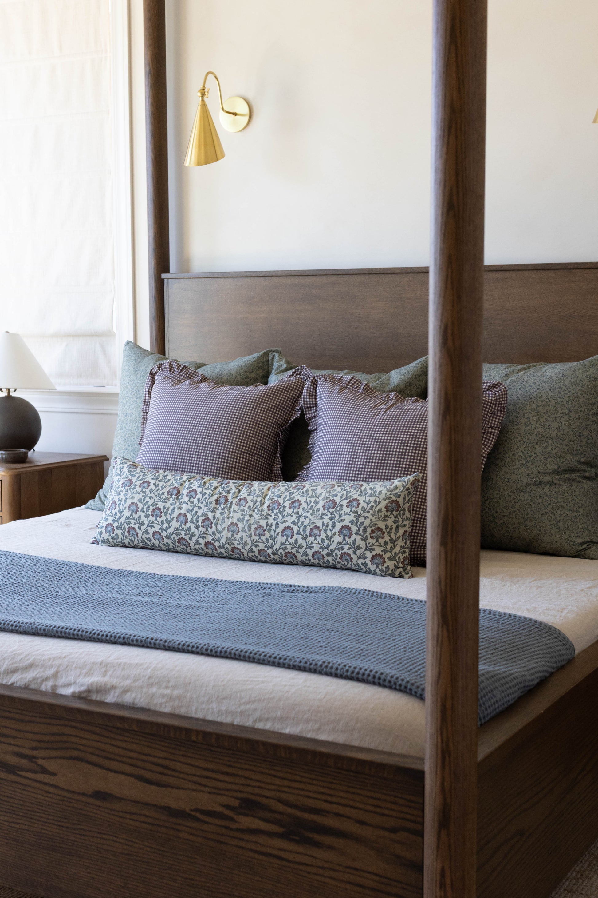 Gold cone-shaped wall sconce with curved arm mounted above wooden bed with multicolor pillows.