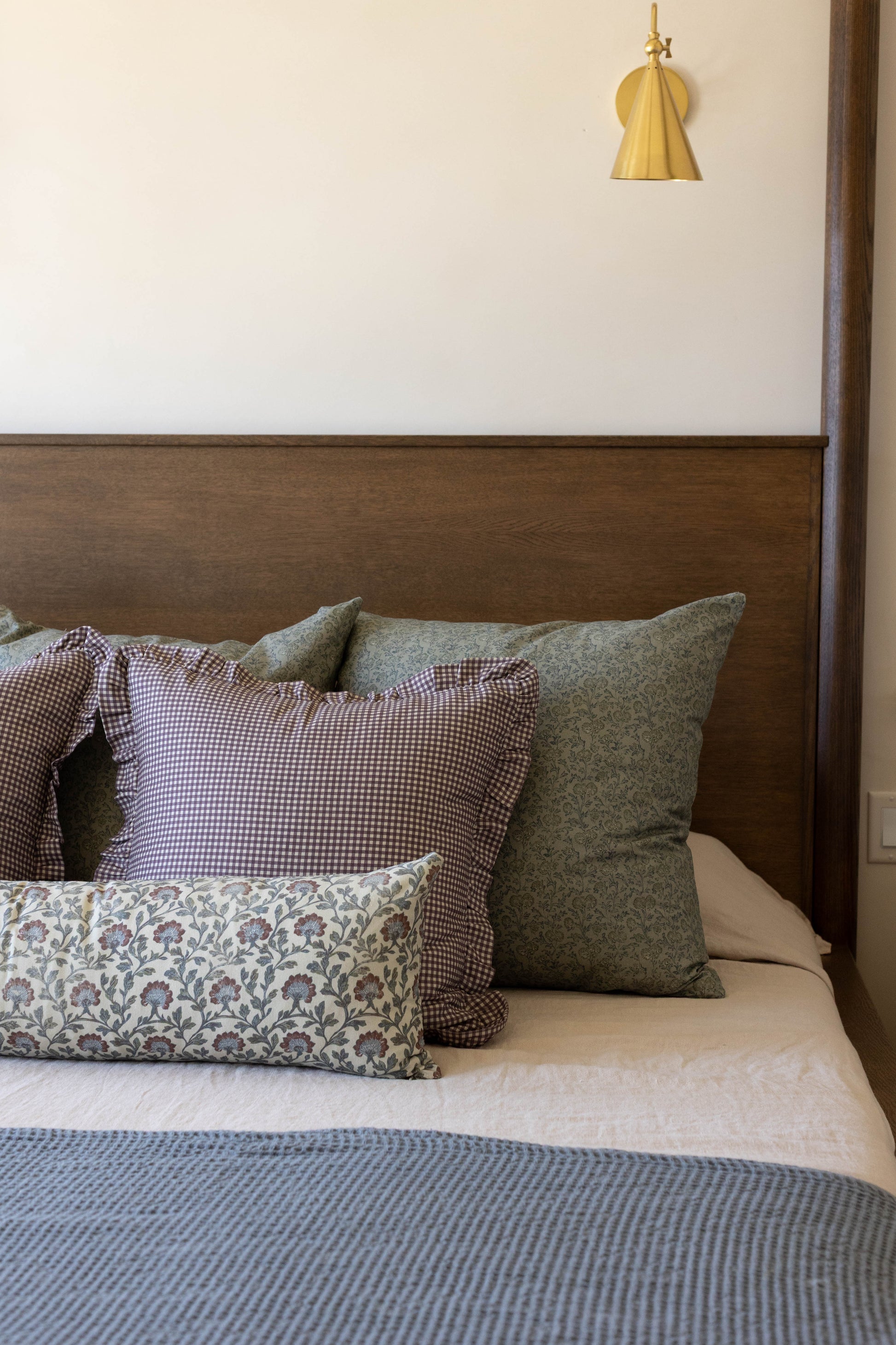 Brass bell-shaped pendant light hanging above a bed with wood headboard and patterned pillows.
