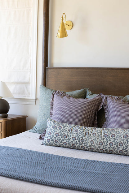 Plum mini gingham ruffle pillow with ruffled edges displayed on a bed with coordinating pillows and bedding.
