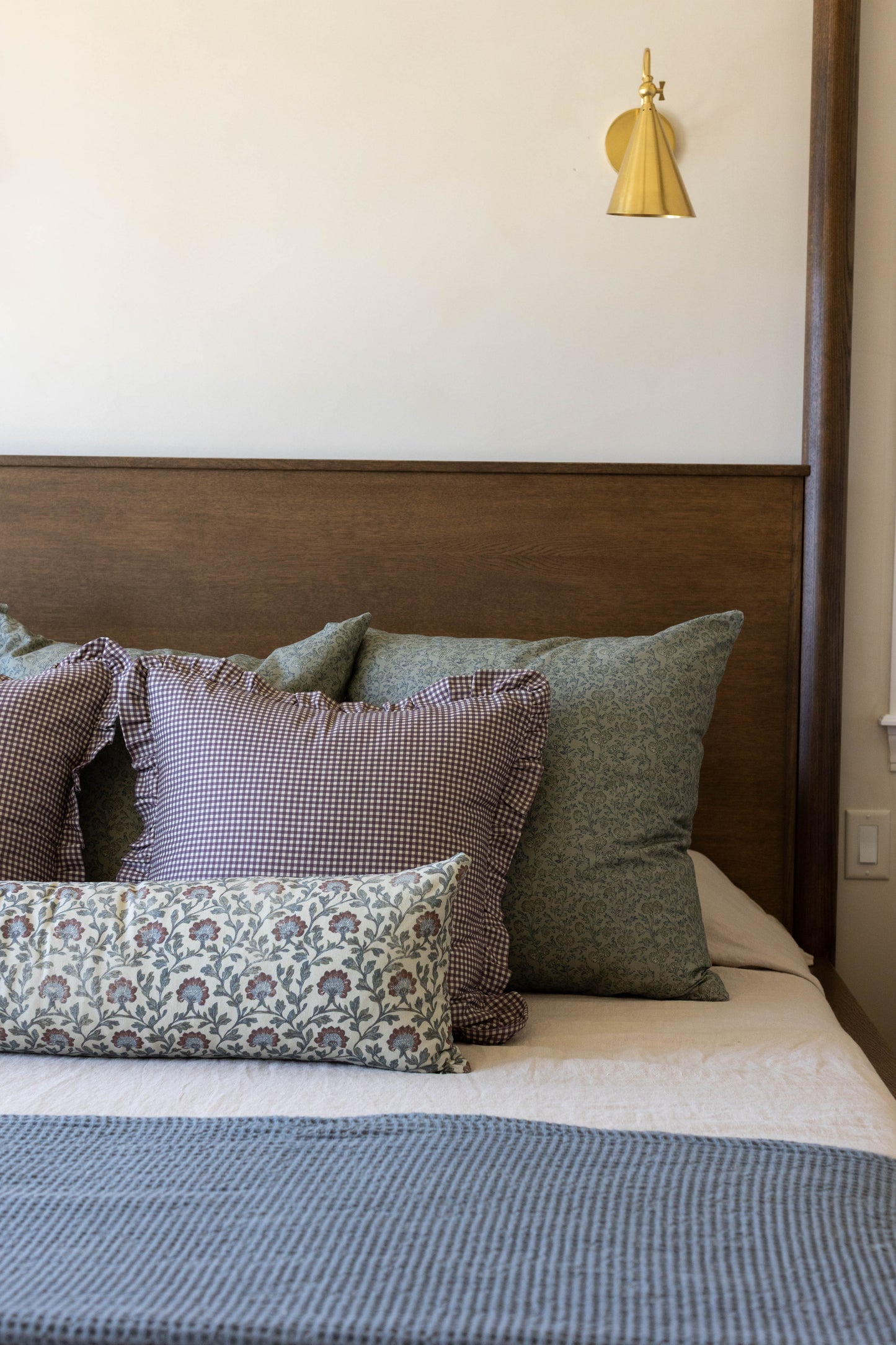 Plum and white mini gingham pillow with ruffled edges displayed on a bed with coordinating decorative pillows.