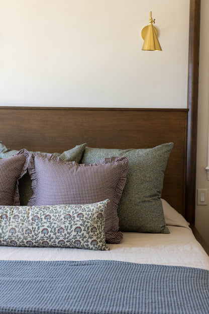 Plum and white mini gingham pillow with ruffled edges displayed on a bed with coordinating decorative pillows.