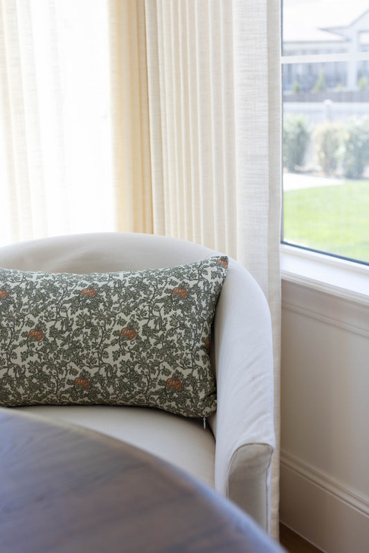 Rectangular throw pillow with green and cream floral pattern featuring gourd and ivy motifs, displayed on a white armchair.