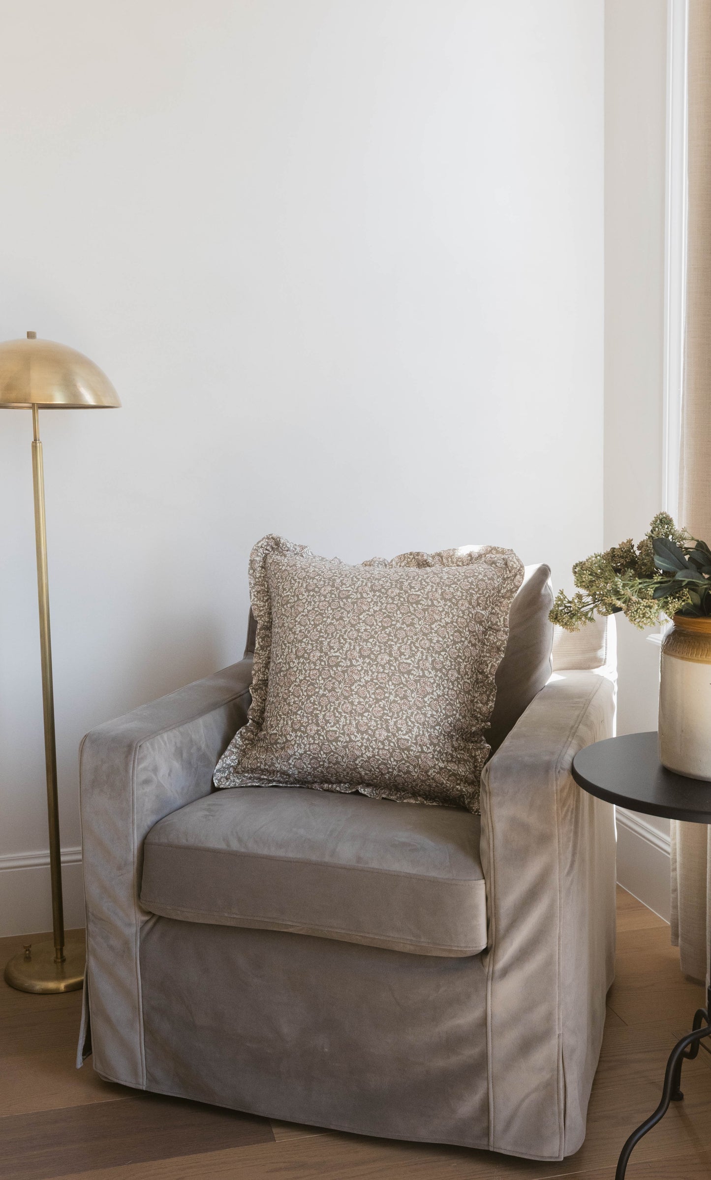 Beige patterned square pillow with ruffled edges displayed on a gray upholstered armchair.