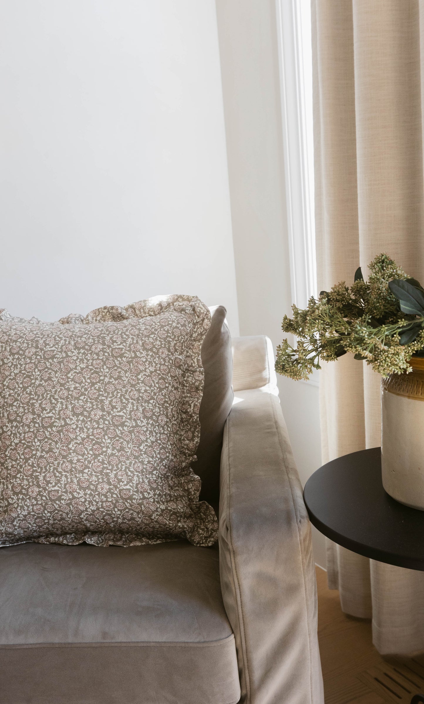 Beige patterned pillow with ruffled edges displayed on a cream upholstered chair.