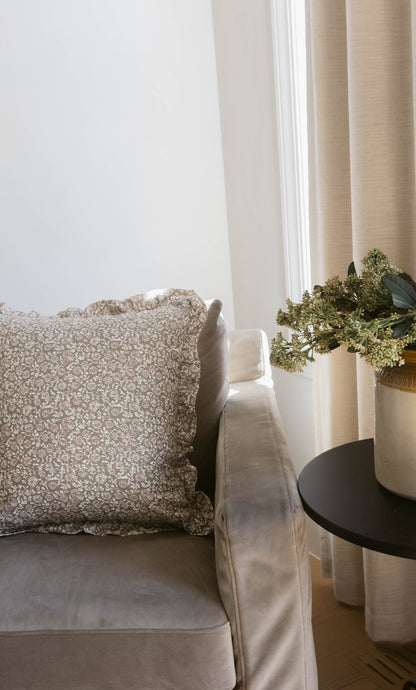 Beige patterned pillow with ruffled edges displayed on a cream upholstered chair.