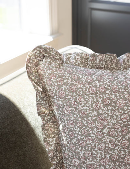 Tan and cream floral patterned pillow with ruffled edges draped over a neutral upholstered chair.