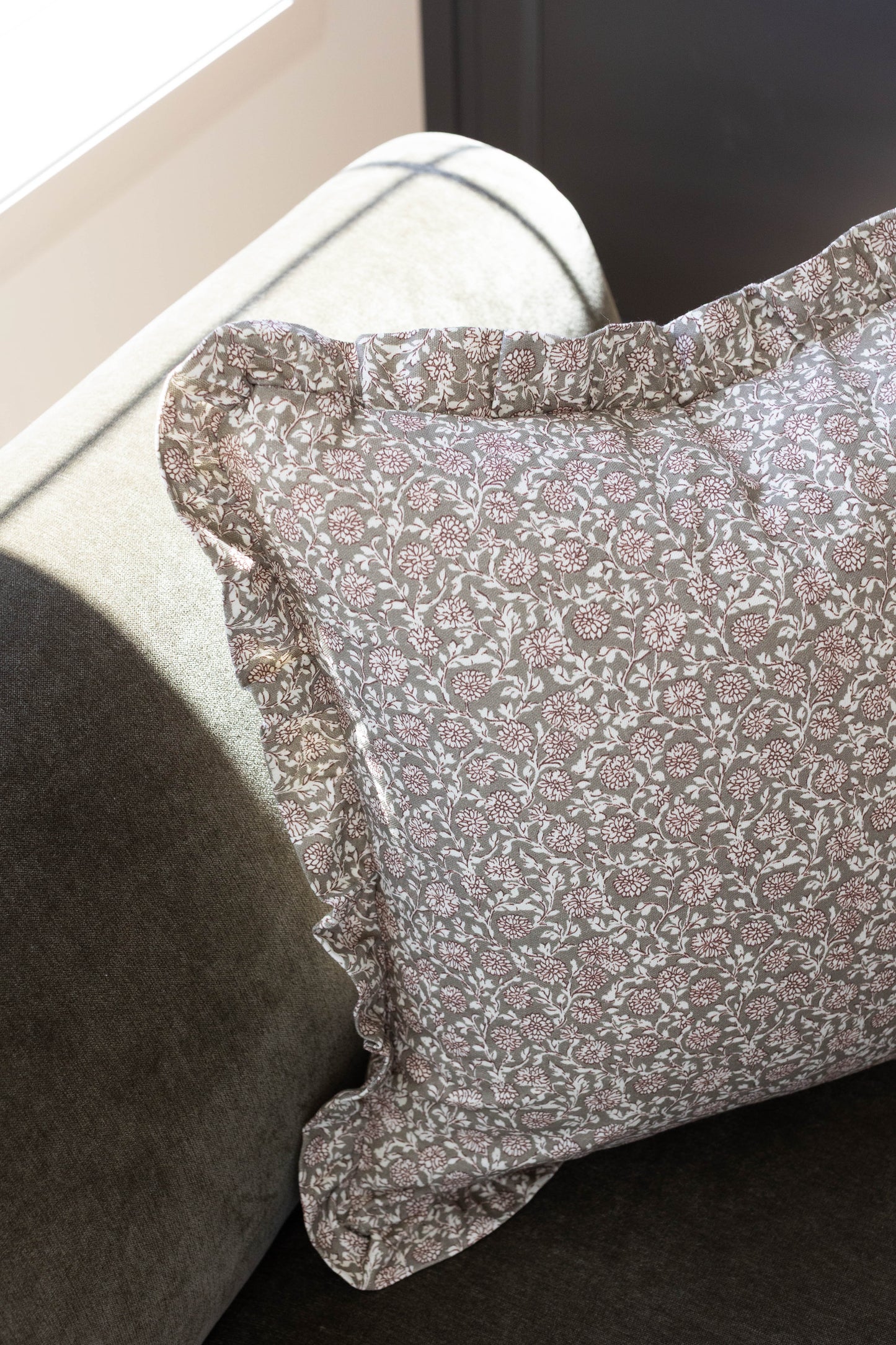 Taupe and white floral patterned pillow with ruffled edge detail on cream-colored furniture.