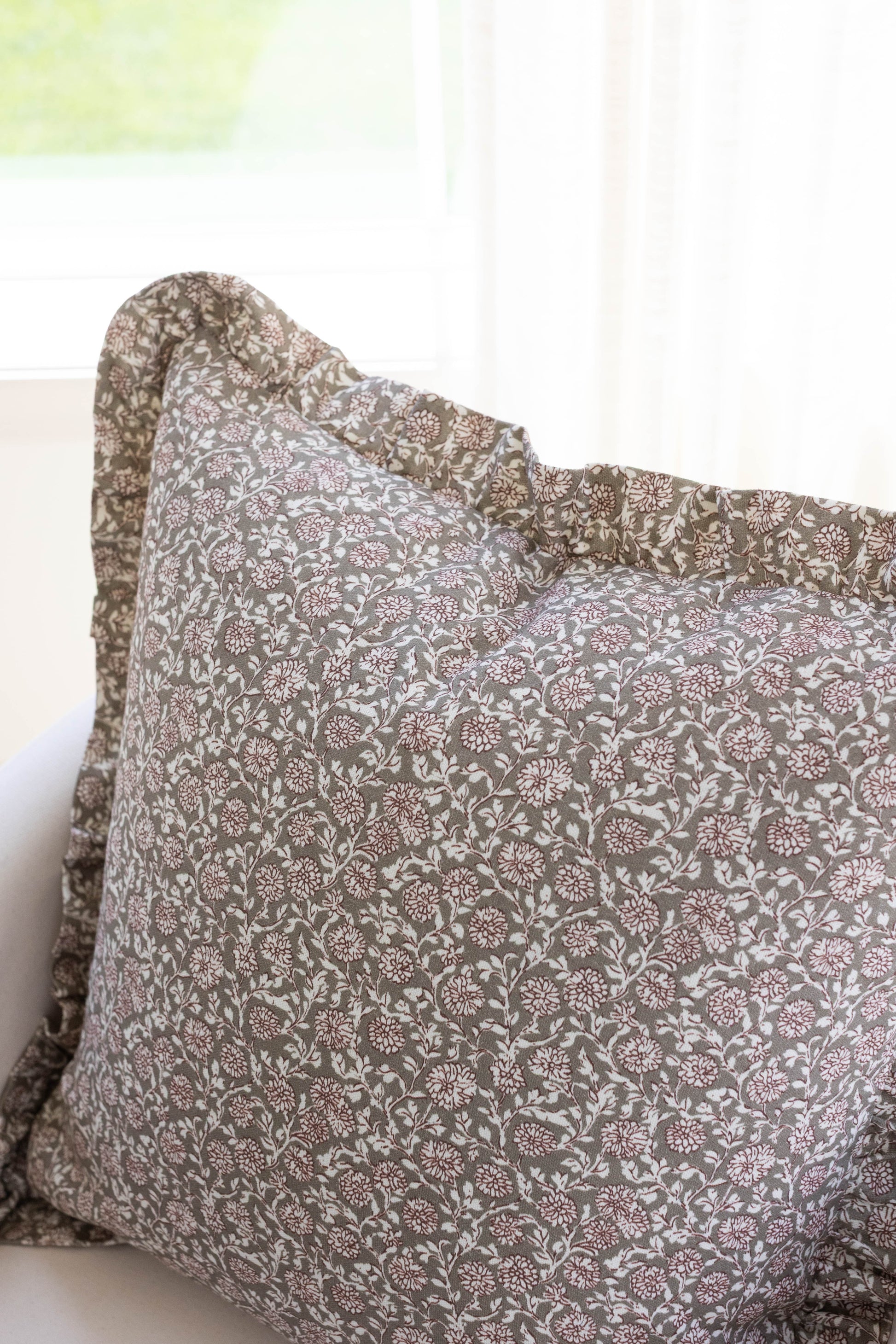 Taupe and white floral patterned pillow with ruffled edges.