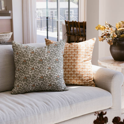 Two decorative pillows on a cream sofa: one with gray floral pattern, one with tan checkered pattern.