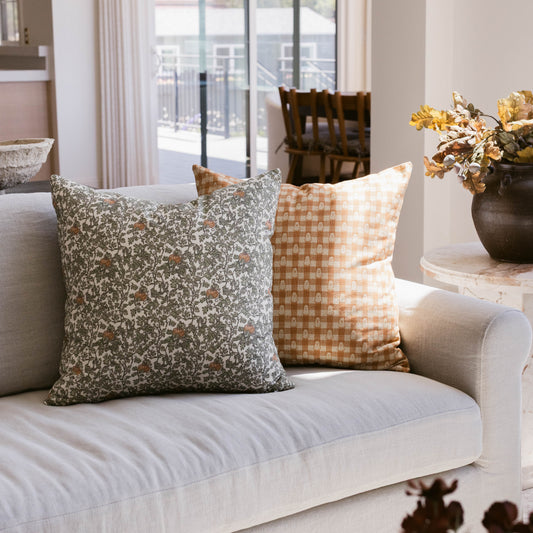 Two decorative pillows on a cream sofa: one with gray floral pattern, one with tan checkered pattern.