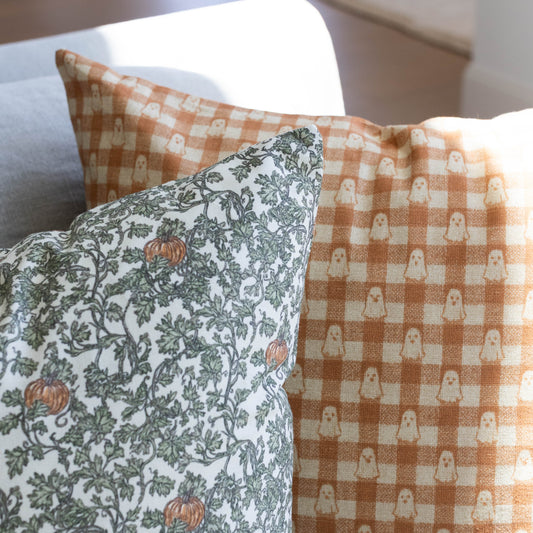 Two throw pillows: one with cream background featuring green ivy and orange gourds, one with tan and cream gingham check patt