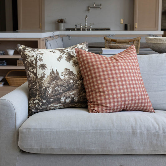 Coral and cream gingham plaid throw pillow displayed on a gray sofa.