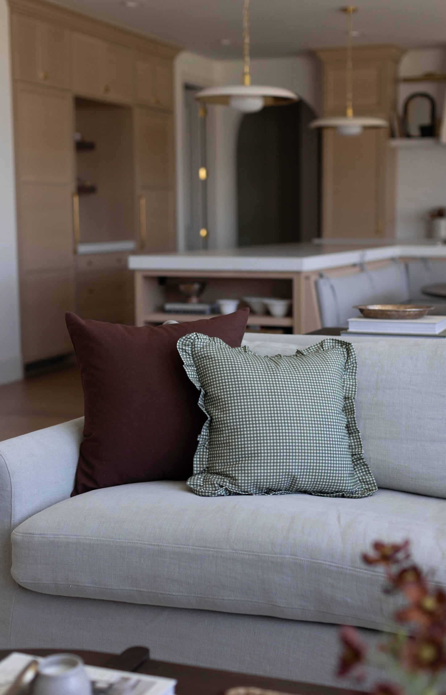 Light gray upholstered sofa with dark brown and green gingham patterned throw pillows in a neutral kitchen-living space.