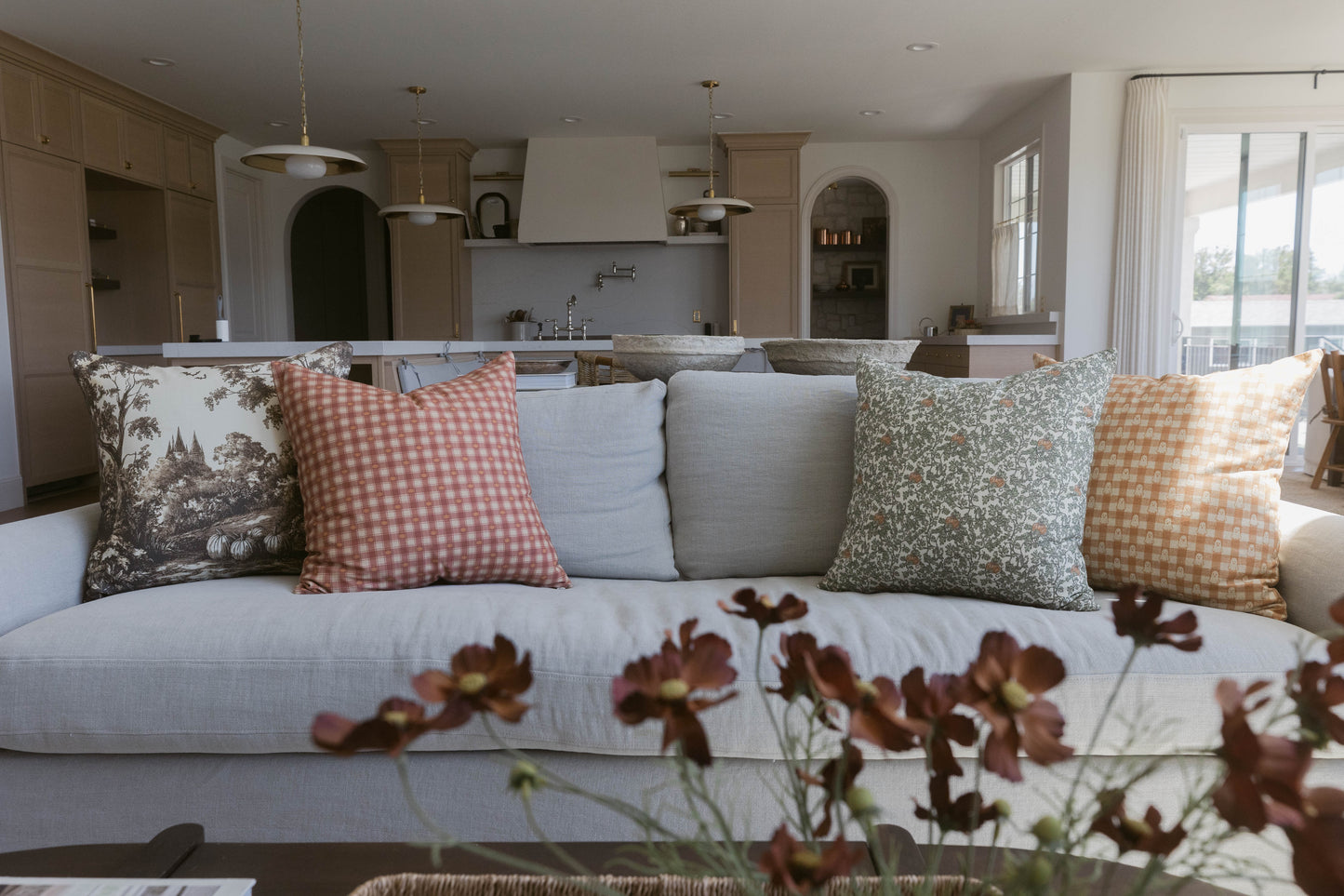 Four decorative pillows in varying patterns displayed on a light gray sofa in a kitchen-living space.