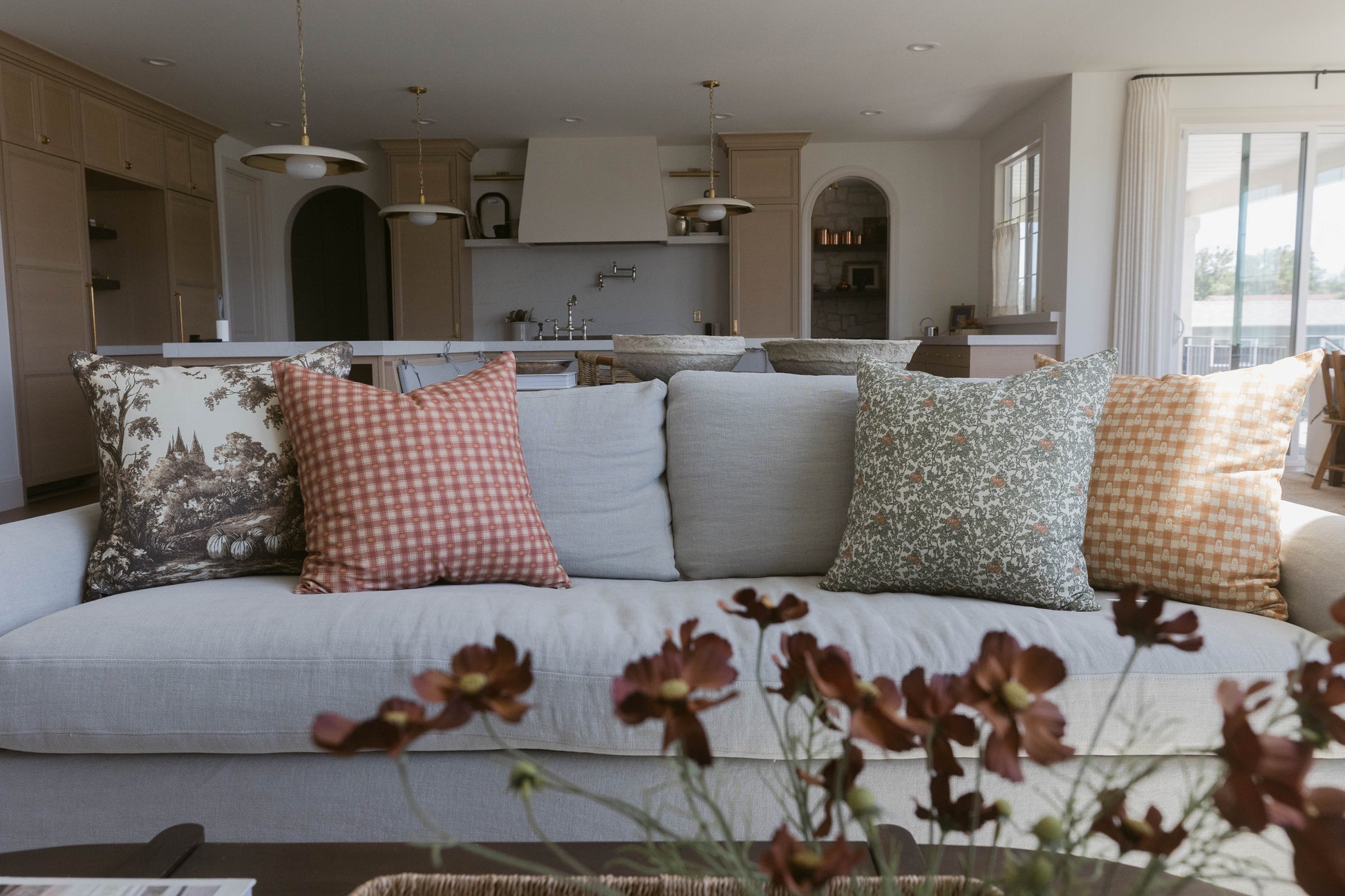 Four decorative pillows in varying patterns displayed on a light gray sofa in a kitchen-living space.